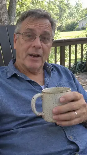 An older actor sits on a back deck holding a speckled mug and talks to the camera, an ad for a coffee subscription.
